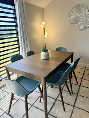 Un coin repas comprenant une table en bois, quatre chaises, une plante en pot, un luminaire fixé au mur et un élément décoratif mural.