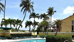 A swimming pool with lounge chairs, palm trees, and a building with a red roof. - Family Retreat @Palm 5 Golf View (Palmas del Mar)