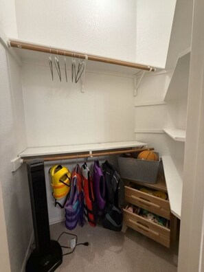 Un dressing avec un porte-chaussures, des sacs suspendus et un petit meuble de rangement.