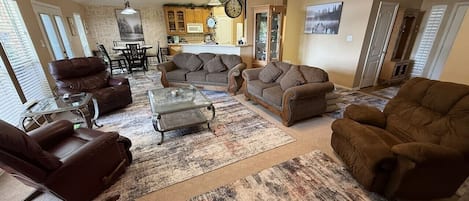 A spacious living room with a fireplace, leather sofas, a coffee table, and a dining area with a chandelier.