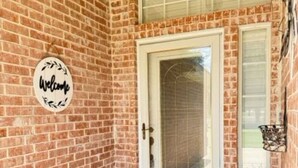 A brick exterior with a white door, a welcome sign, and a small potted plant. - Oasis at Eagle Mountain Lake (Azle)