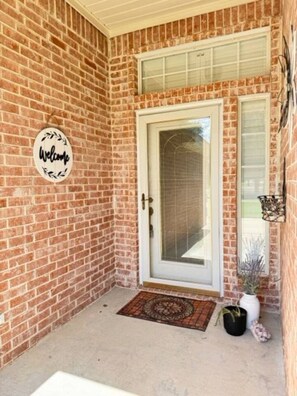 A brick exterior with a white door, a welcome sign, and a small potted plant. - Oasis at Eagle Mountain Lake (Azle)