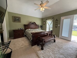 A bedroom with a bed, a nightstand, a chair, a ceiling fan, and a window with curtains. - Oasis at Eagle Mountain Lake (Azle)