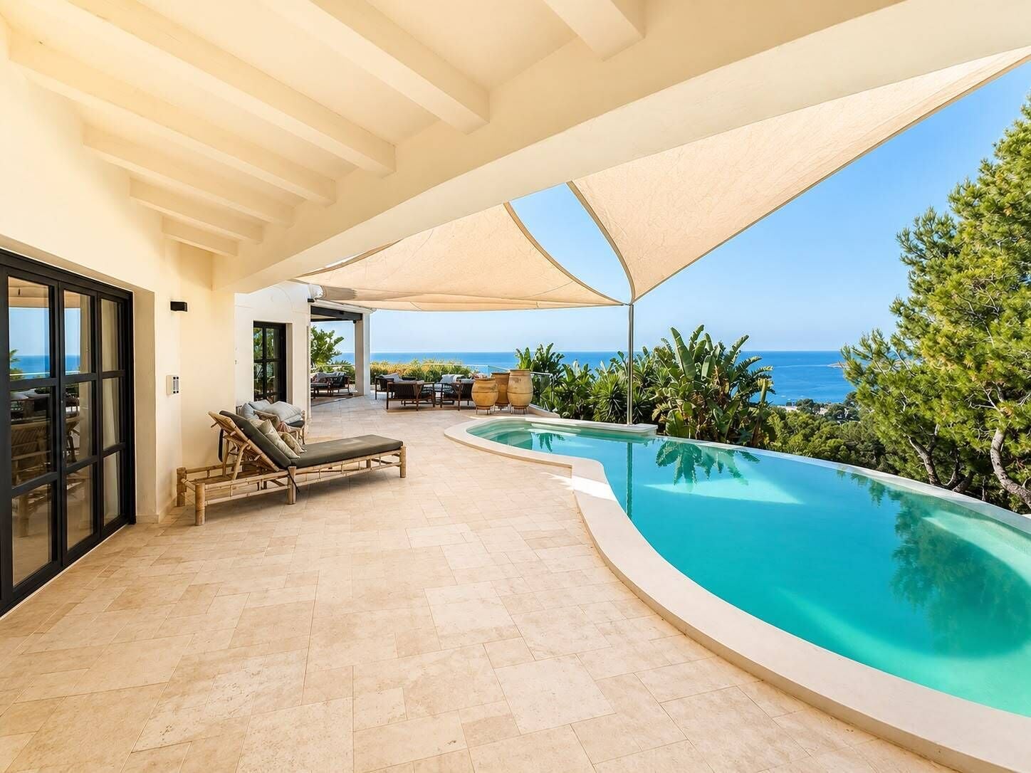 A pool area with lounge chairs, a covered seating area, and a view of the ocean.