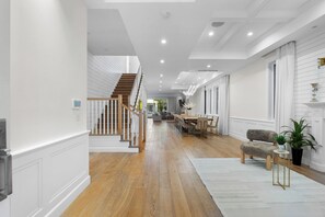 Ein geräumiger Flur mit einer Holztreppe, einem Essbereich mit einer Chandelieber und einem Wohnzimmer mit einer Couch und Pflanzen.