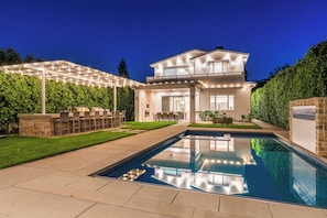 A two-story house with a swimming pool, outdoor seating, and a well-maintained garden.