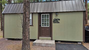 Une petite cabane avec une porte marron et un logo représentant un ours, entourée d’arbres.