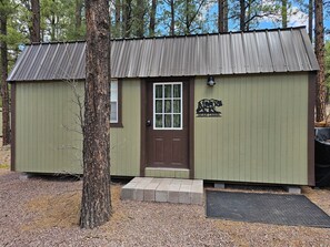 A small cabin with a brown door and a bear logo, surrounded by trees.