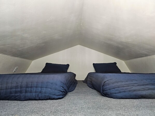 A small, sloped ceiling room with two beds and a single wall-mounted light fixture.