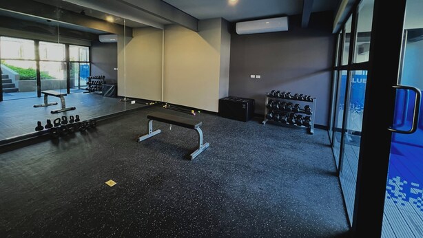 Una palestra con uno specchio a parete, una panca, manubri e un tapis roulant.