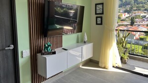 Un soggiorno moderno con una TV a schermo piatto fissata alla parete, un mobile bianco sottostante e un balcone con vista su una zona residenziale.