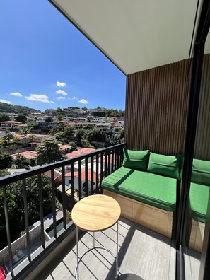 Ein Balkon mit grünen Sitzmöbeln, einem kleinen runden Tisch und Blick auf eine Wohngegend.