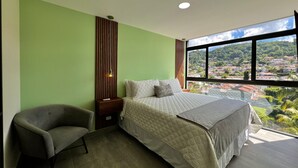 Una camera da letto con un letto, una sedia, un comodino, una finestra vista città e un muro con linee verticali.