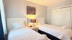 A hotel room with two beds, a nightstand with a lamp, a painting on the wall, and a white wardrobe. - Modern Myrtle Beach Getaway|2BR Condo |Pool&Tennis (Myrtle Beach)