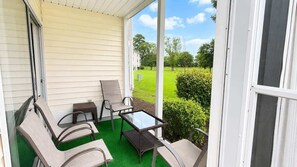 A covered porch with outdoor furniture and a view of a green lawn and trees. - Modern Myrtle Beach Getaway|2BR Condo |Pool&Tennis (Myrtle Beach)