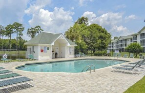 A swimming pool with lounge chairs, a small building with a gabled roof, and a fenced area with trees. - Modern Myrtle Beach Getaway|2BR Condo |Pool&Tennis (Myrtle Beach)