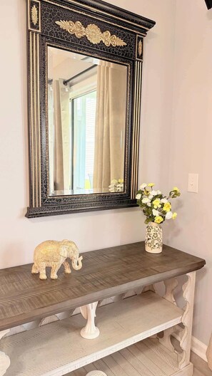 Een spiegel met een versierde zwarte lijst, een decoratief olifantje en een vaas met bloemen op een houten consoletafel.