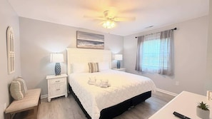 Ein Schlafzimmer mit Bett, Nachttischen, einer Bank, einem Deckenventilator und einem Fenster mit Vorhängen.