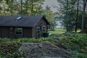 Une cabane avec un toit en pente, une cheminée et une fenêtre donnant sur une zone herbeuse.