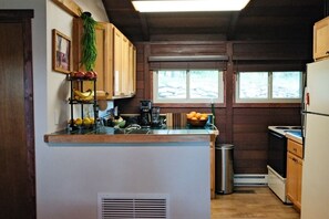 A kitchen with wooden cabinets, a central island with fruit, a window, and a stove. - Serene 2-Bedroom Lakeview Cabin Retreat w/ Dock, Kayak & SUP with AC (Central City)