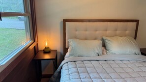 Een slaapkamer met een bed, nachtkastje, lamp en raam.