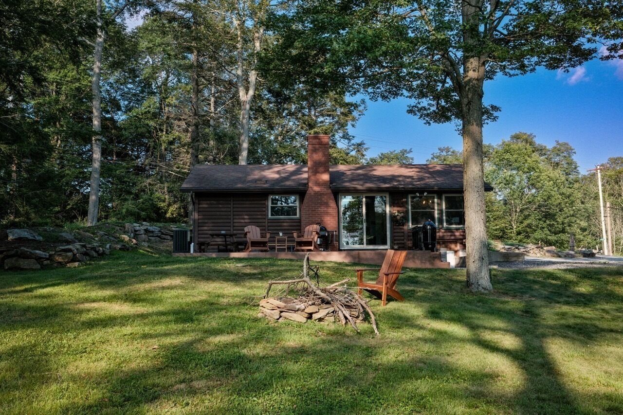 A cabin with a chimney, a deck with chairs, and a fire pit in the yard.