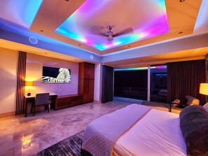 A modern hotel room with a large bed, a desk, a chair, a television, and a ceiling fan. - EXCLUSIVE GATED LUXURY • PANORAMIC OCEAN & SUNSET VIEWS • PRIME PV (Puerto Vallarta)
