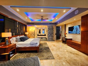Ein modernes Hotelzimmer mit einem großen Bett, einem Deckenventilator, einem Flachbildfernseher und einem durchgehenden Türspalt sichtbaren Badezimmer.