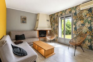 A modern living room with a sofa, a wooden coffee table, a fireplace, and a large window with a view of greenery. - L'Ardèchoise - Piscine - Petfriendly (Vallon-Pont-d'Arc)