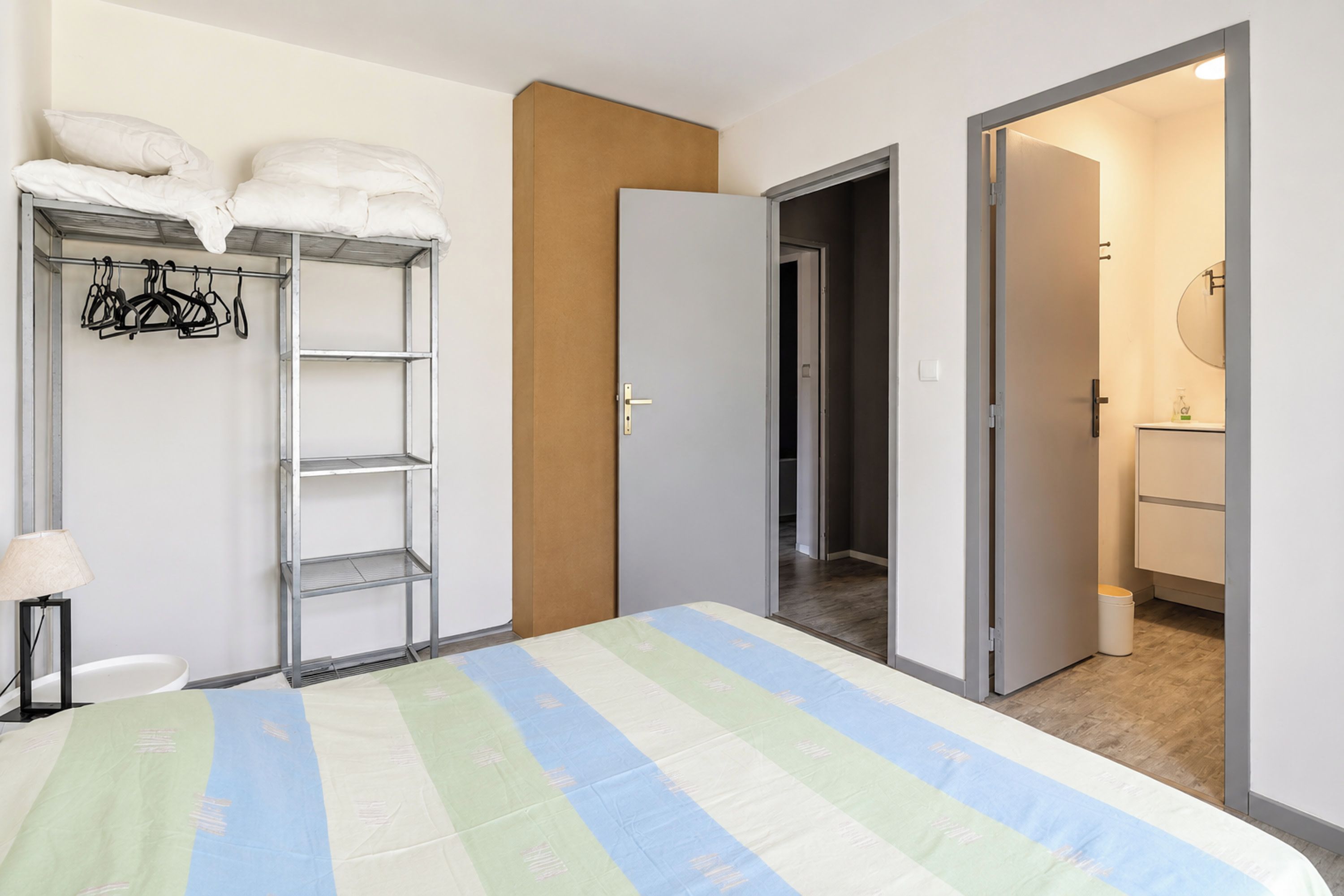 A bedroom with a bed, a wardrobe, a shelf with hangers, and a door leading to a bathroom.