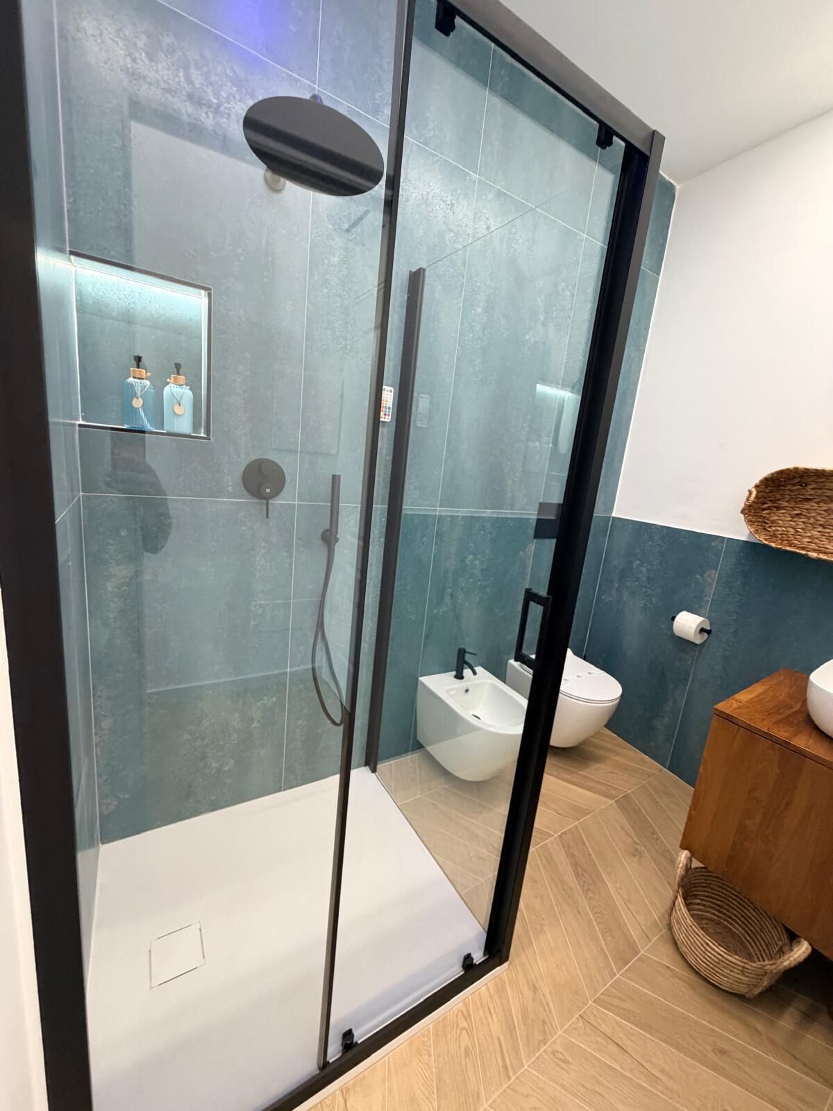 Une salle de bain moderne avec une douche à parois de verre, un bidet et un meuble-lavabo en bois.