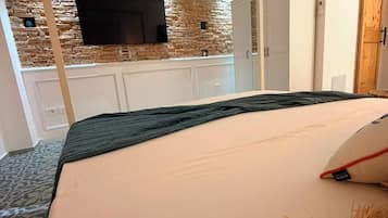 Une chambre d’hôtel comprenant un lit, un téléviseur fixé au mur, une armoire et un coin cuisine avec un mur en pierre.