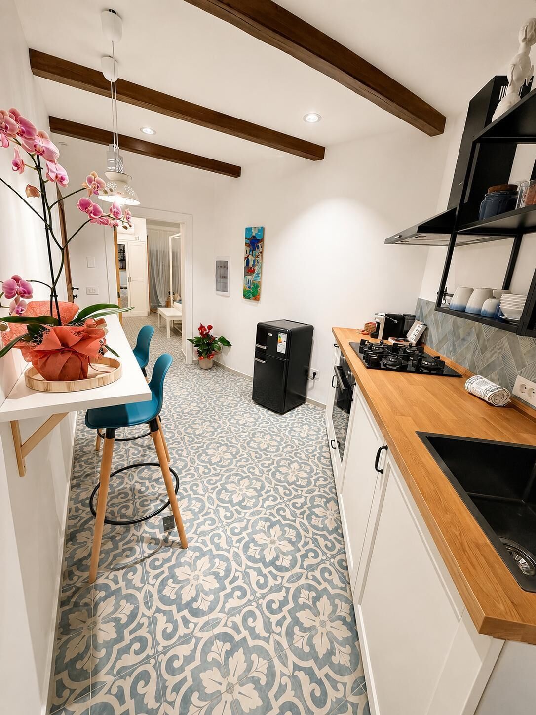 Una cocina moderna con mostrador de madera, refrigerador negro y comedor con mesa blanca y sillas azules.