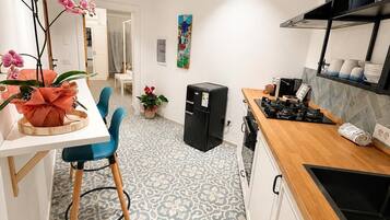 Una cocina moderna con mostrador de madera, refrigerador negro y comedor con mesa blanca y sillas azules.