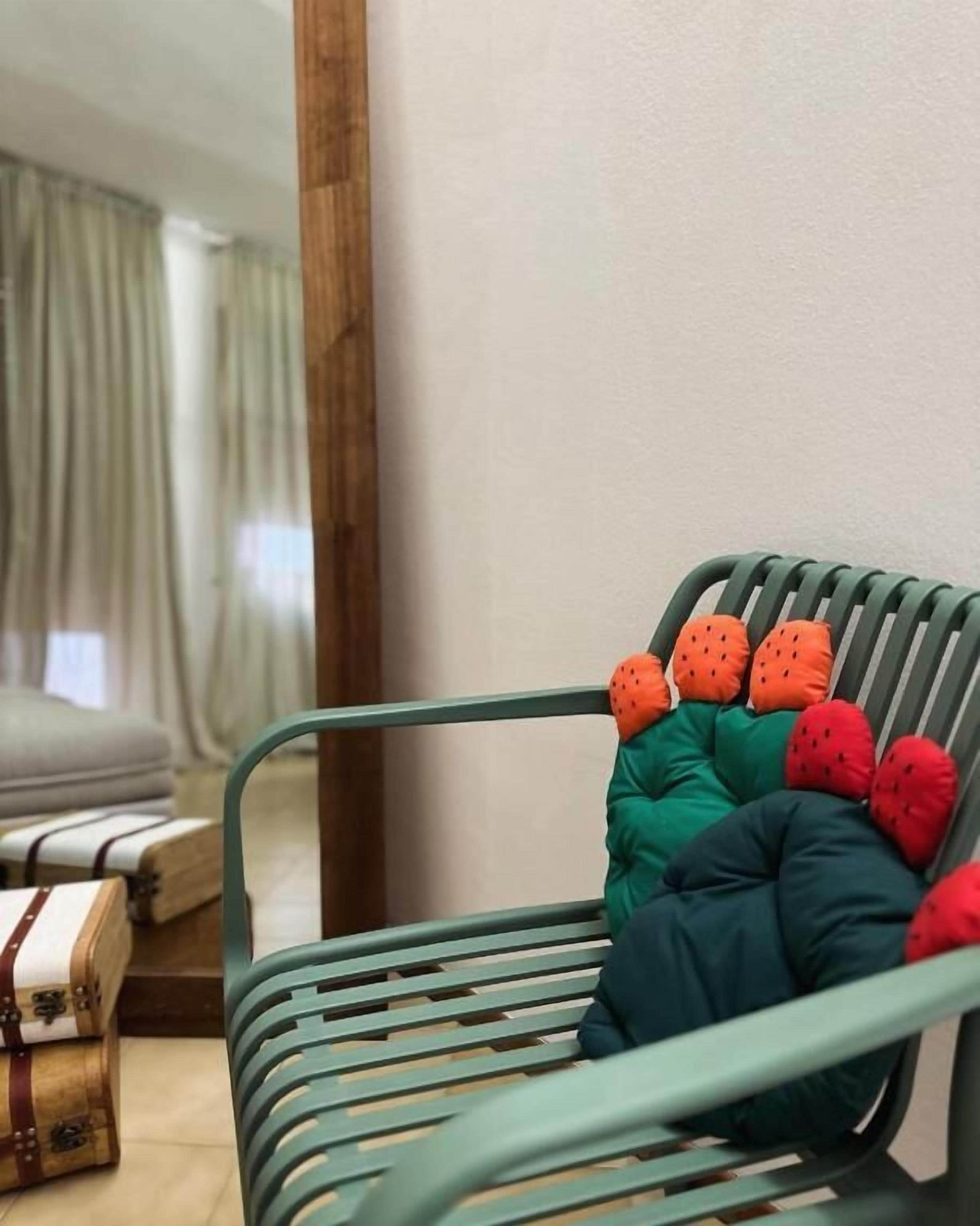 Una silla metálica verde con cojines de colores junto a una pared.