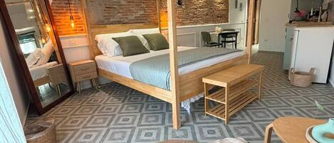 A room with a four-poster bed, a small table, a chair, and a kitchenette area.
