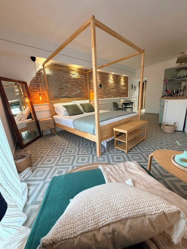 A room with a four-poster bed, a small table, a chair, and a kitchenette area.