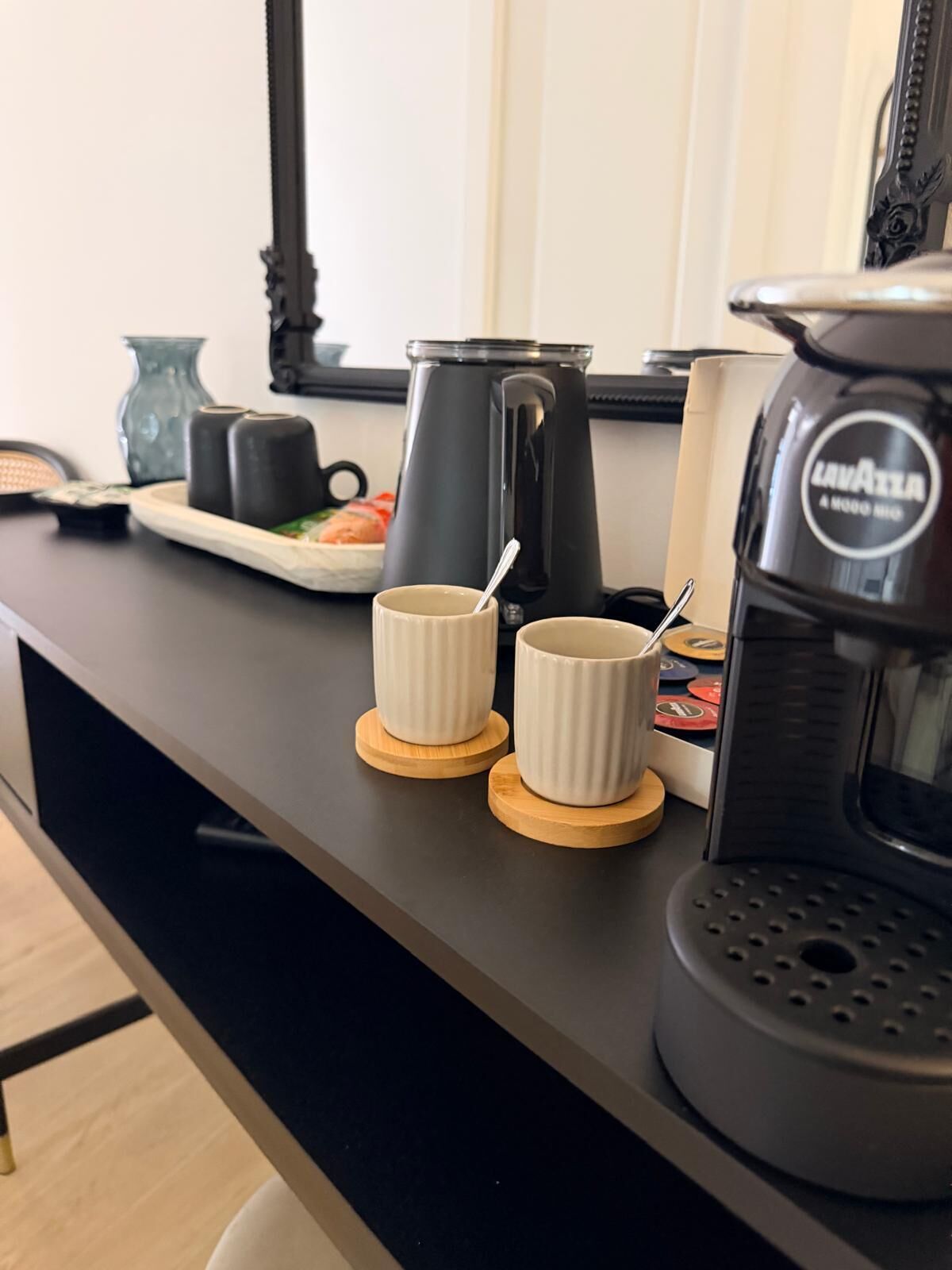 A kitchen counter with a coffee maker, two white mugs, a plate with food, and a kettle.