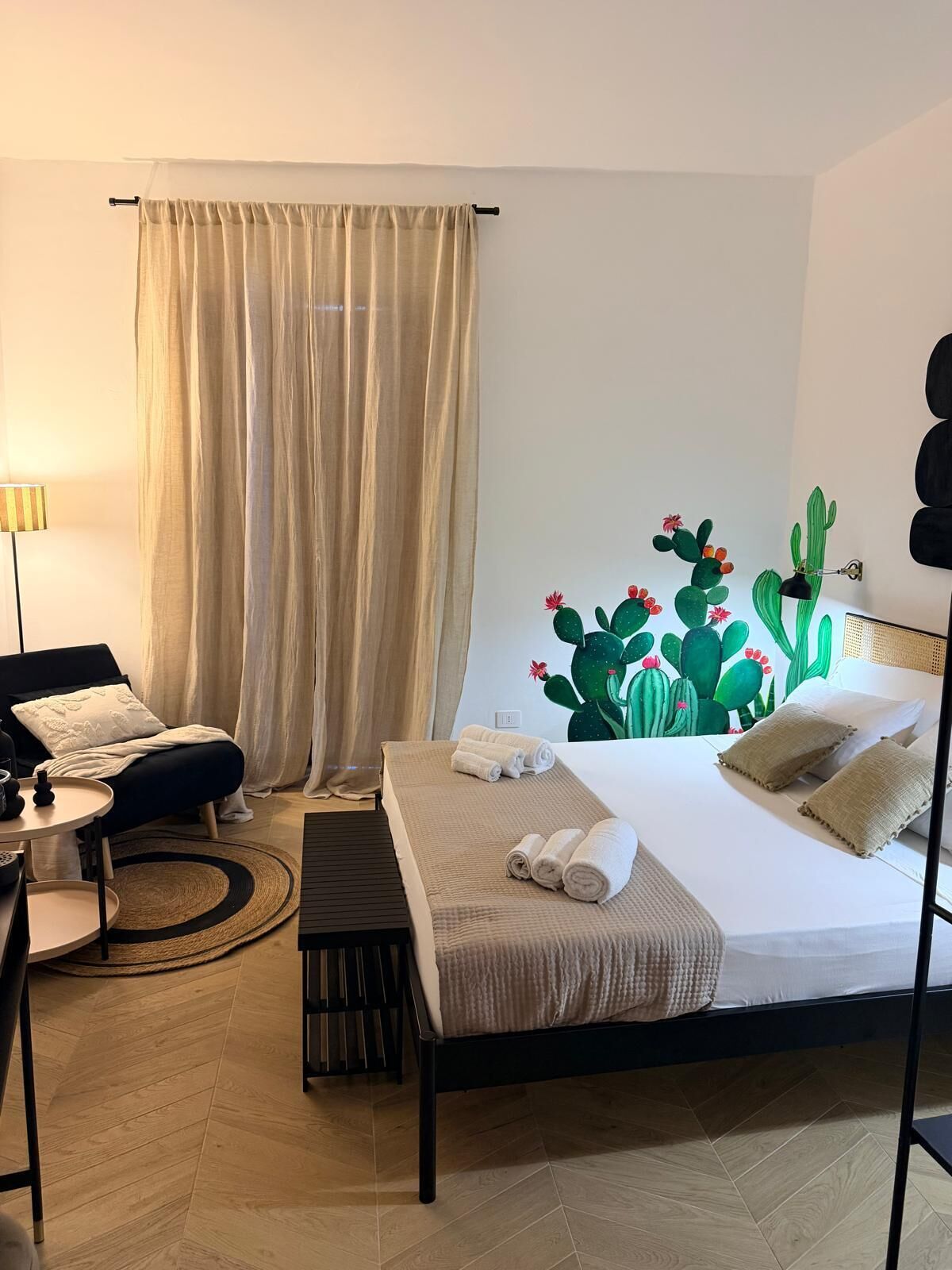 A hotel room with a bed, a desk, a chair, a lamp, and a wall mural.