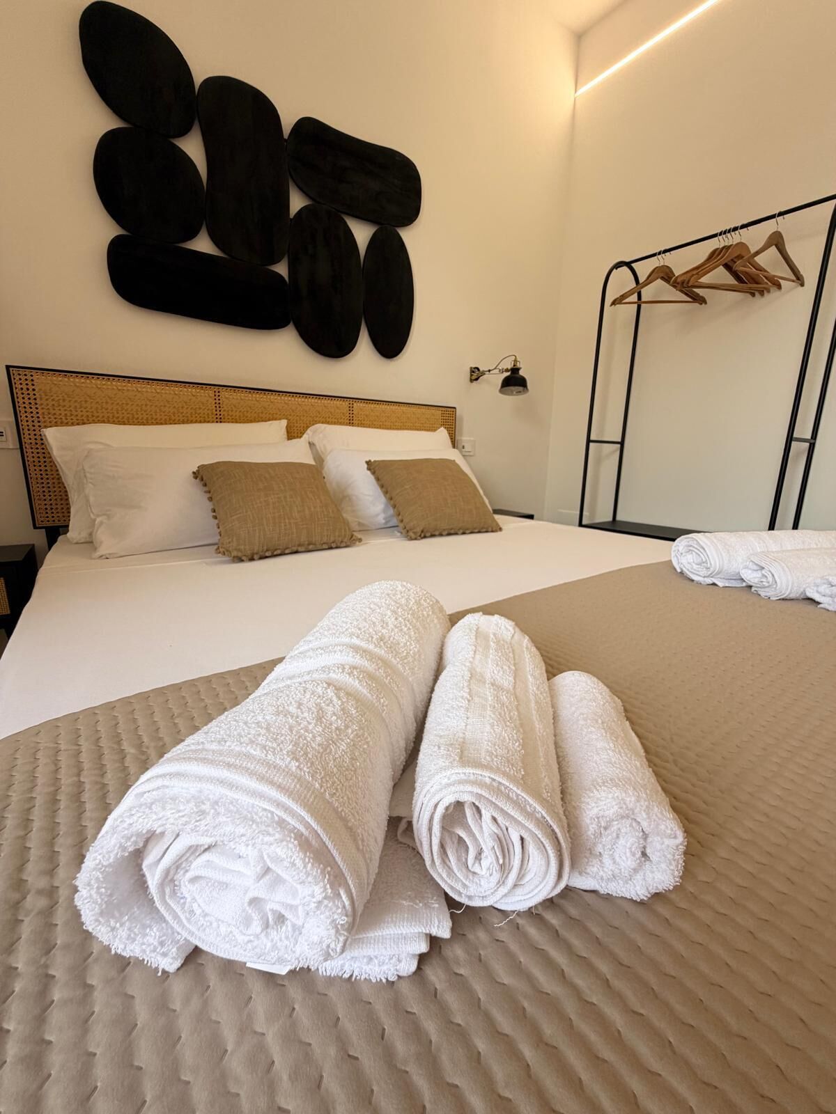 A neatly made bed with rolled towels, a headboard, and a wall-mounted towel rack.