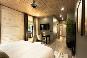 A bedroom with a large bed, a desk with a chair, a television on the wall, and a potted plant. - New Cabin - Indoor Swim Spa, Hot Tub, Game Room! (Gatlinburg)