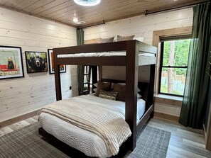 Un lit superposé avec une tête de lit, une fenêtre avec des rideaux et des tableaux encadrés accrochés au mur.