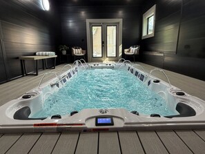 Ein Whirlpool mit Bedienfeld, umgeben von Holzboden, Stühlen und einem Tisch mit Kissen.