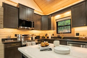 Une cuisine moderne avec des meubles en bois foncé, des appareils électroménagers en acier inoxydable et une fenêtre donnant sur la forêt.