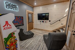 A room with a gaming setup including a large TV, gaming consoles, and a retro Atari sign. - New Cabin - Indoor Swim Spa, Hot Tub, Game Room! (Gatlinburg)