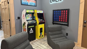 Ett rum med två arkadspel, en väggmonterad skylt med texten ”Game Over”, och två grå fåtöljer.