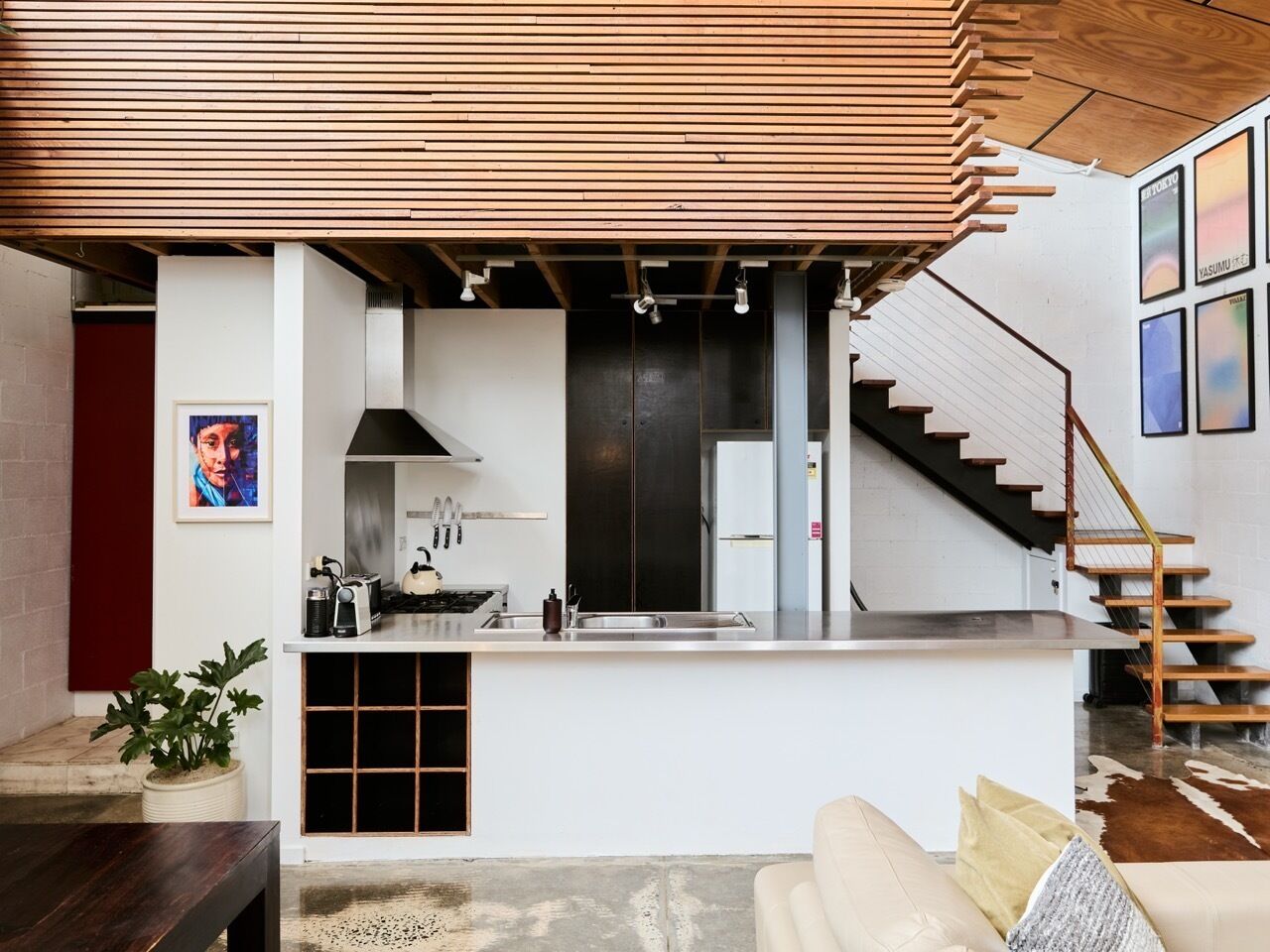 A modern kitchen with a built-in stove, a sink, and a black cabinet. There is a staircase leading to an upper level.