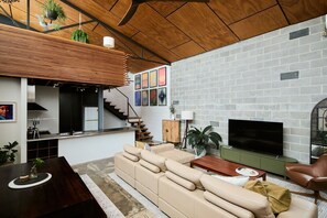 A modern living room with a sectional sofa, a flat-screen TV, and a staircase leading to an upper level. - Bottega Loft Industrial Charm with Artistic Flair (Brunswick)