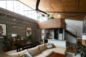 A spacious living area with a sofa, a coffee table, and a dining table. There is a kitchen area with a staircase leading to an upper level. - Bottega Loft Industrial Charm with Artistic Flair (Brunswick)