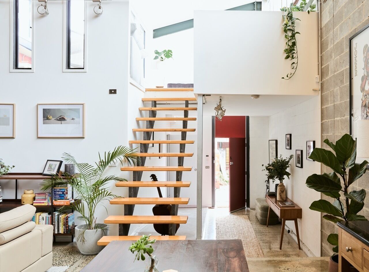 A modern interior with a staircase, bookshelves, and potted plants.